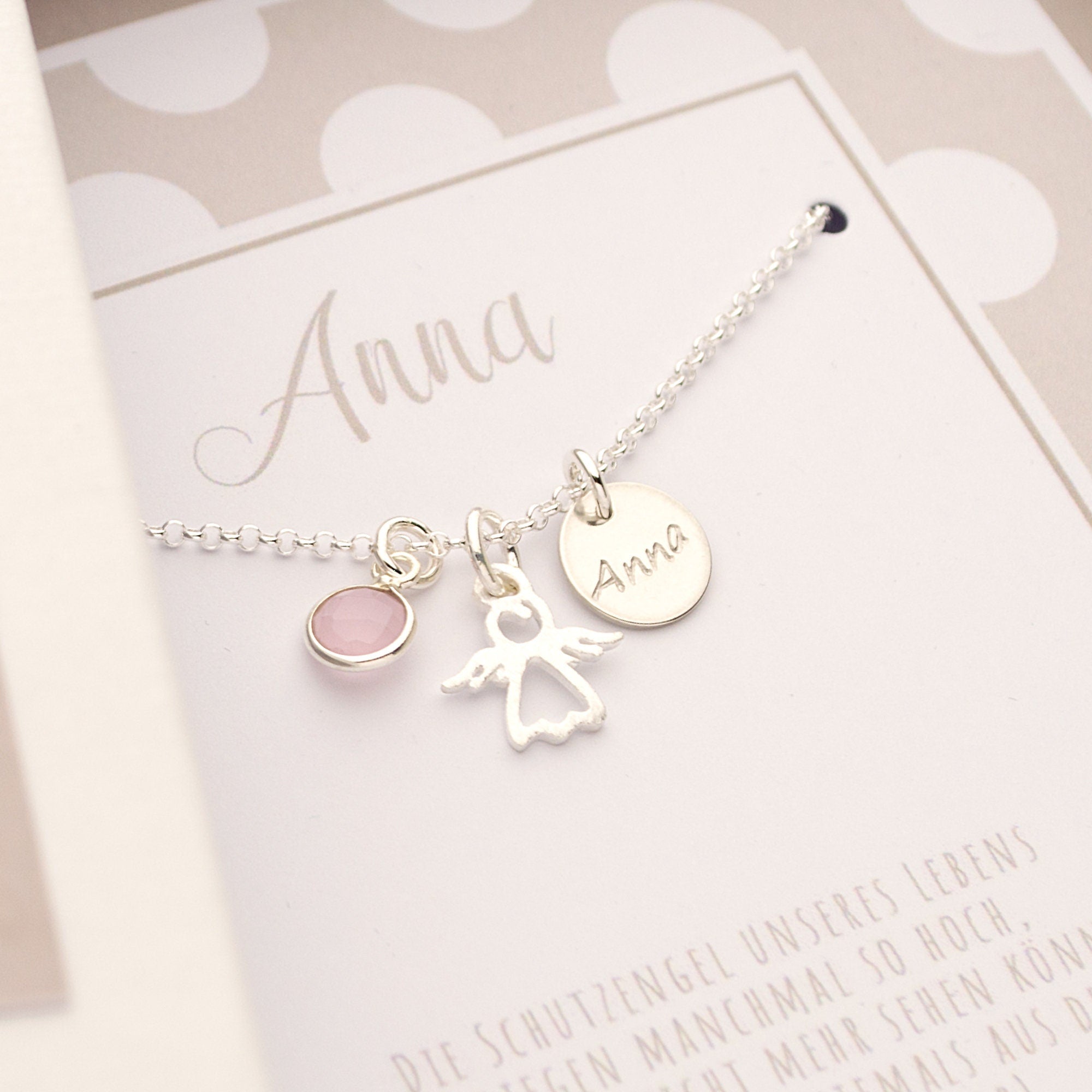 Nahansicht einer Silberkette mit Schutzengel, in Silber gefasstem Rosenquarz und Namens-Anhänger. Die Kette ist in der Geschenkbox montiert.