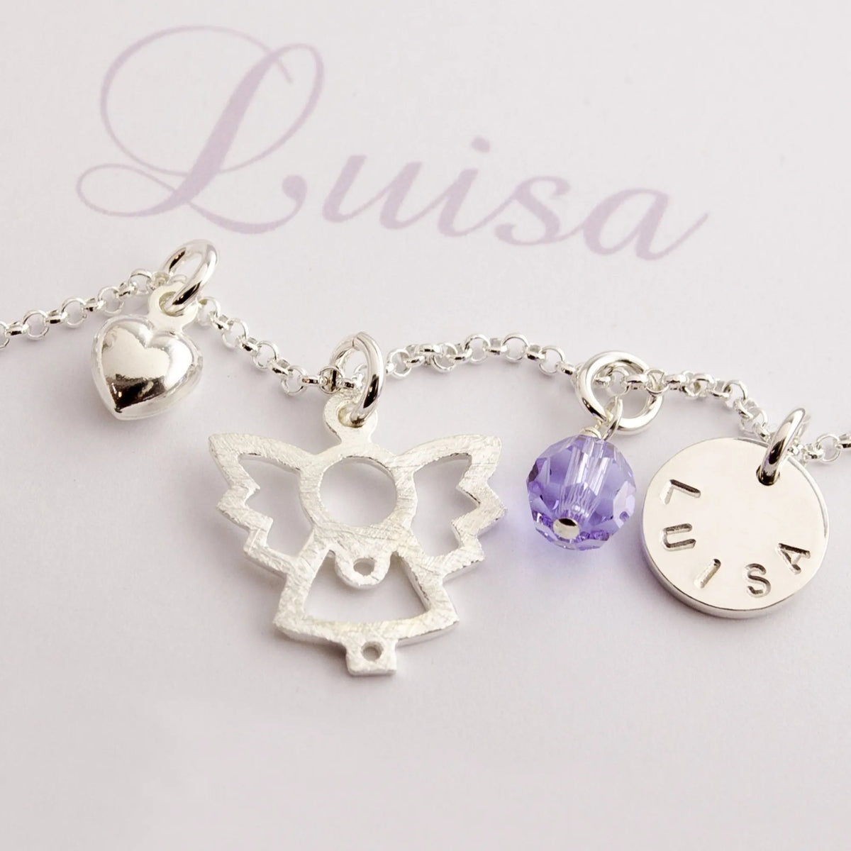 Detailansicht einer filigranen Silberkette mit vier Anhängern: Herz, Engel, Glücksstein in Geburtsstein-Farbe und handgestempeltem Namenstaler aus 925 Sterling Silber.