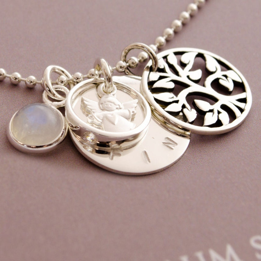 Himmlische Begleiter: Detailansicht der Taufkette "Finn" mit graviertem Namen, Lebensbaum, Engel-Anhänger und schimmerndem Mondstein aus 925 Silber.