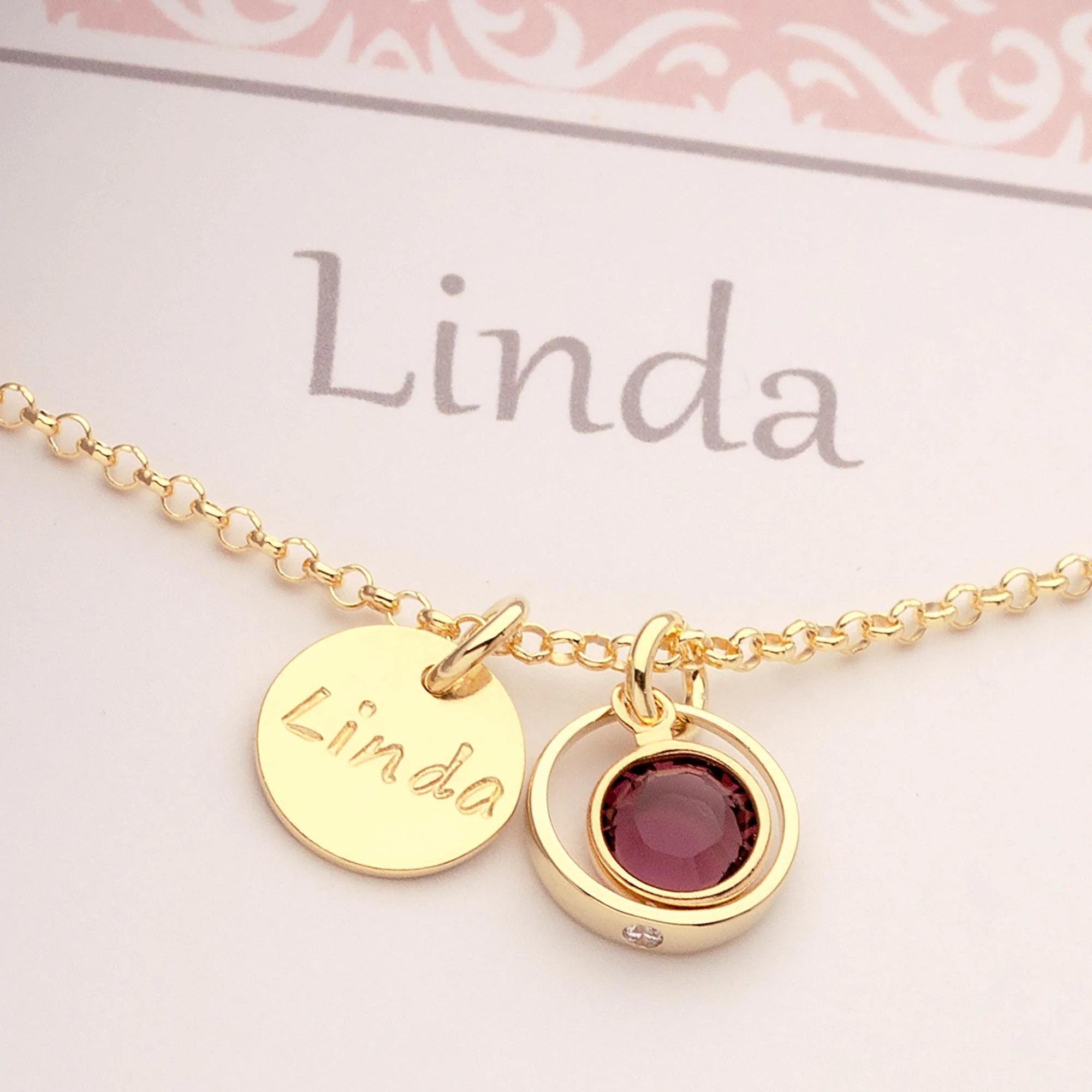 Nahaufnahme einer Gold Taufkette "Linda" mit Namensgravur Taler und lila Amethyst-Geburtsstein in einem zierlichen Taufring mit weißem Zirkon.