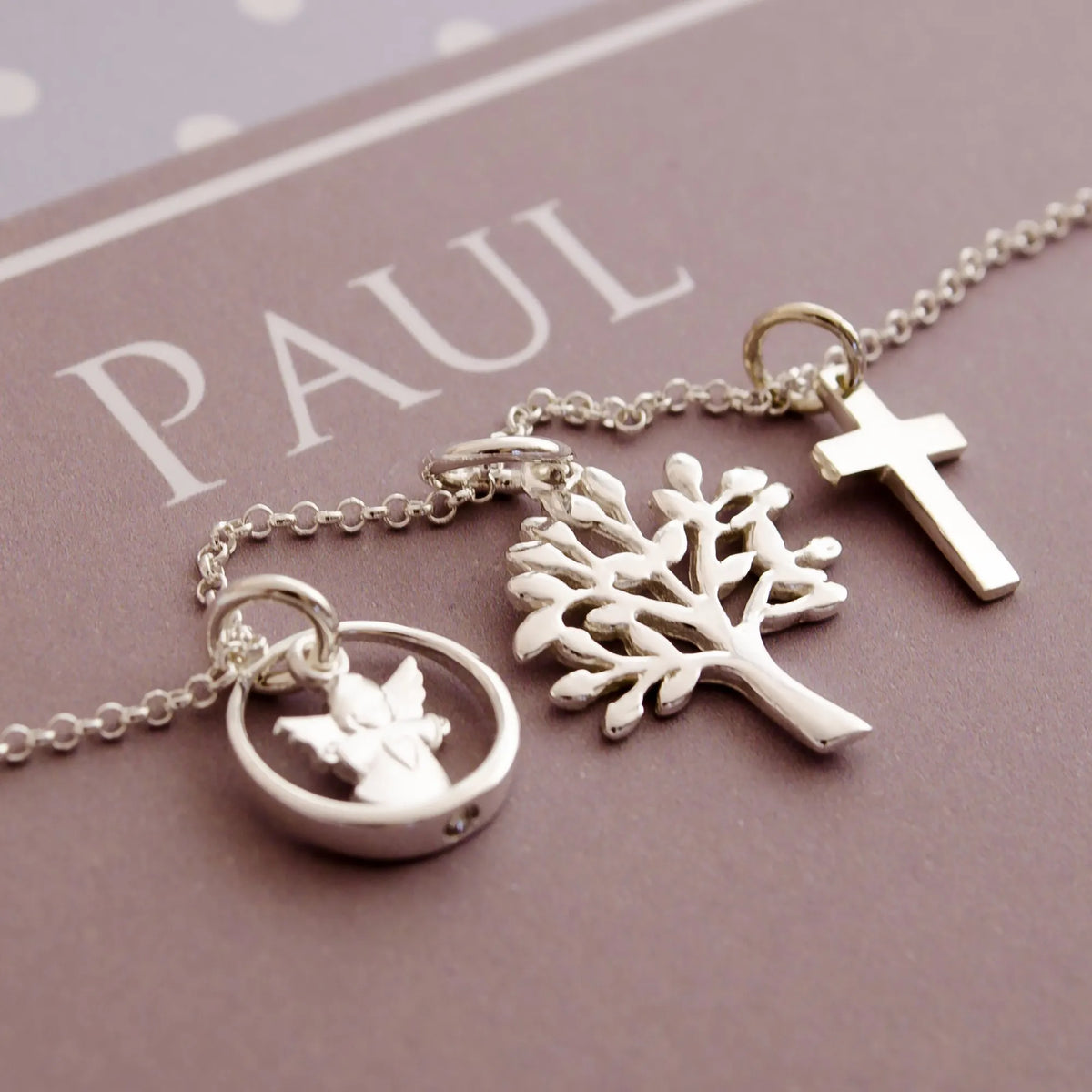 Detailansicht einer filigranen  Silberkette mit Engel im Taufring, Kreuz und Lebensbaum in einer personalisierten Geschenkbox mit Pünktchen-Design in hellblau-taupe-weiß.