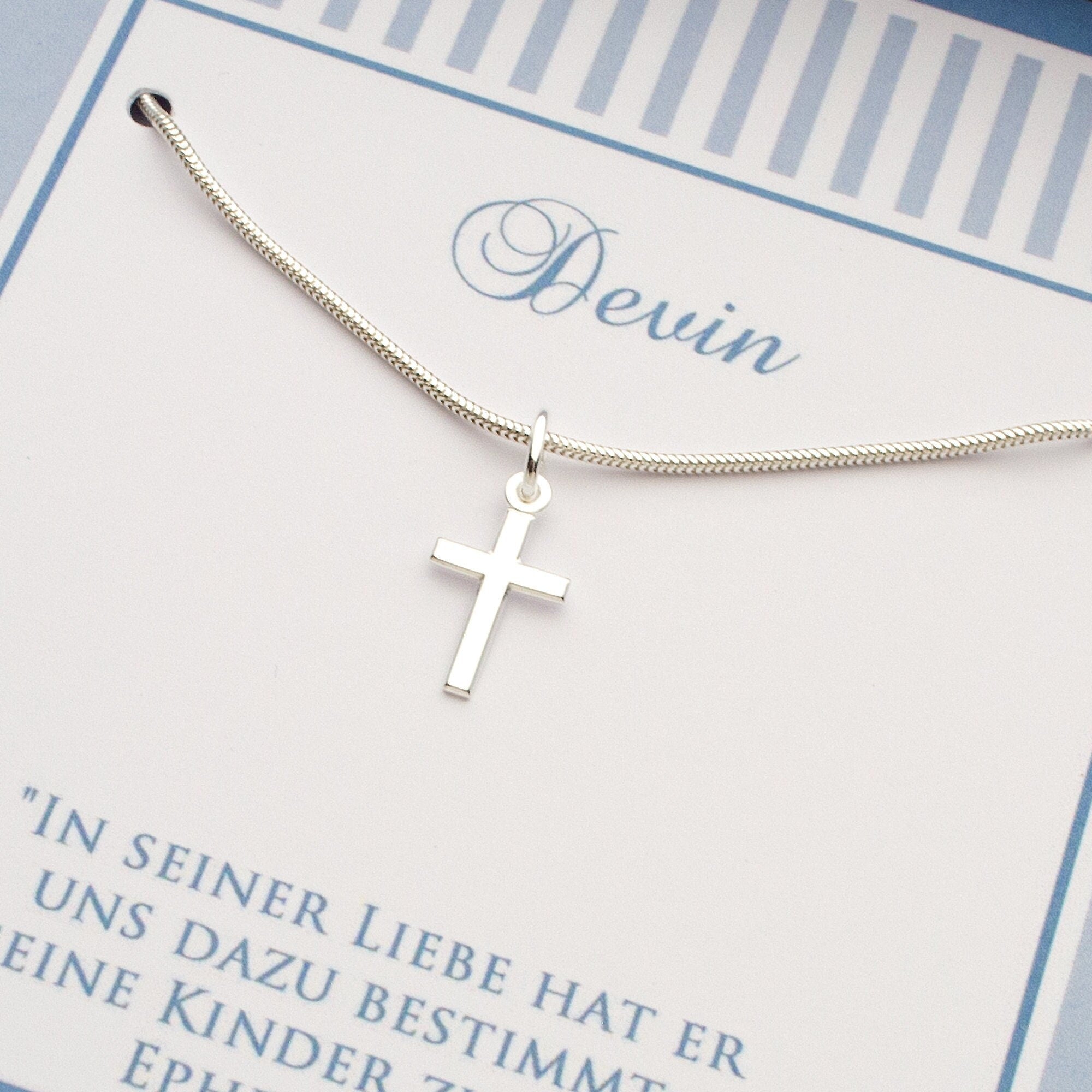 Nahaufnahme einer Taufkette aus 925 Silber mit klassischem Kreuz-Anhänger an einer eleganten Schlangenkette. Liegt auf einer personalisierten Karte mit dem Namen 'Devin' und einem Taufspruch. Von Bloomgart.