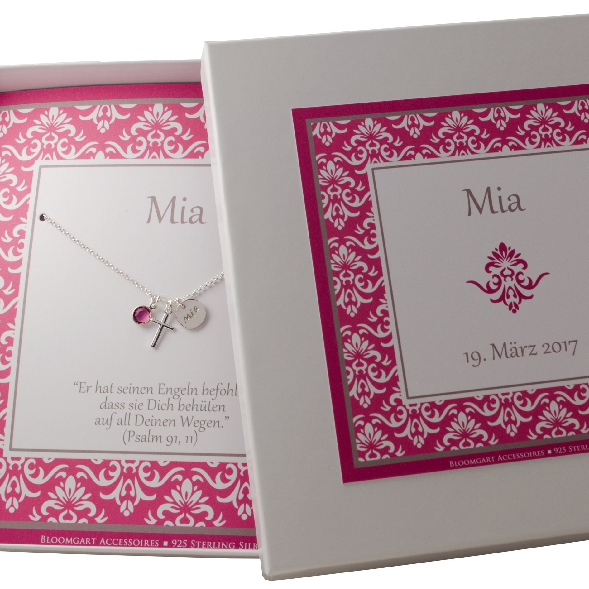 Eine Silberkette mit Kreuz, Namens-Anhänger und Kreuz in einer personalisierten Geschenkbox mit Ornament-Muster in himbeer Farbton. Innenliegend befindet sich die Kette mit dem Namen 'MIA' und Taufspruch: 'Er hat seinen Engeln befohlen, dass sie dich behüten auf all deinen Wegen.' Psalm 91,11