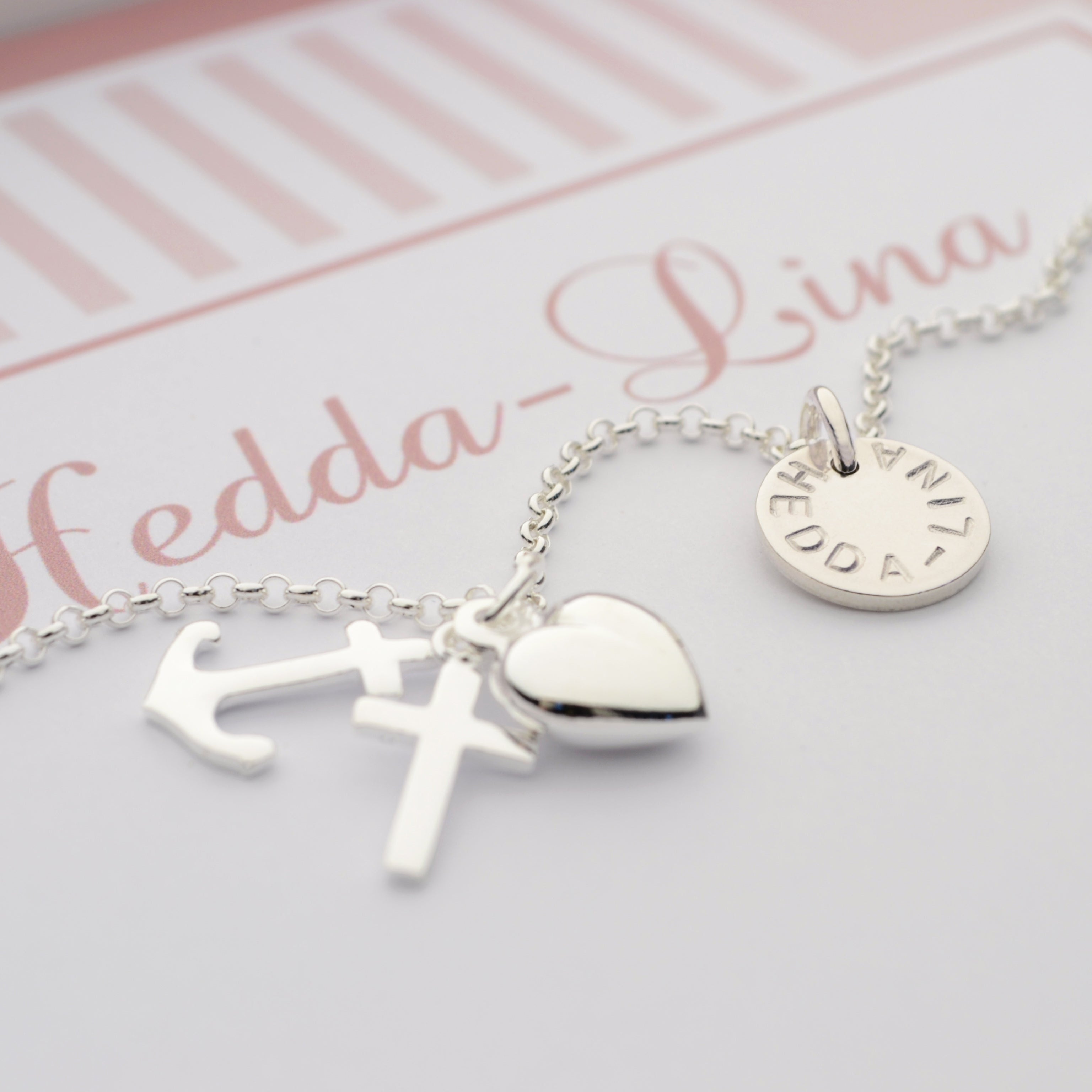 Personalisierte Halskette aus 925 Sterling Silber mit Anhängern für Glaube (Kreuz), Liebe (Herz) und Hoffnung (Anker) sowie einem Gravurplättchen mit dem Namen "Hedda-Lina". Die Kette liegt in einer personalisierten Geschenkbox.