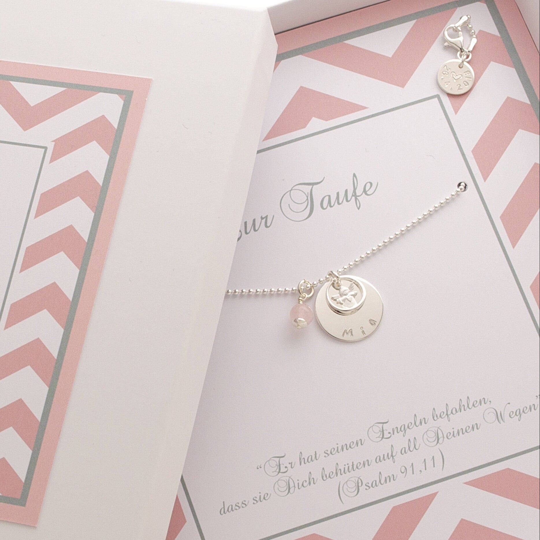 Detailansicht eines personalisierten Taufgeschenks in einer rosa-weißen Geschenkbox mit persönlichem Taufspruch und Taufkette mit Namenstaler, Engel, Taufring und Rosenquarz-Anhänger.