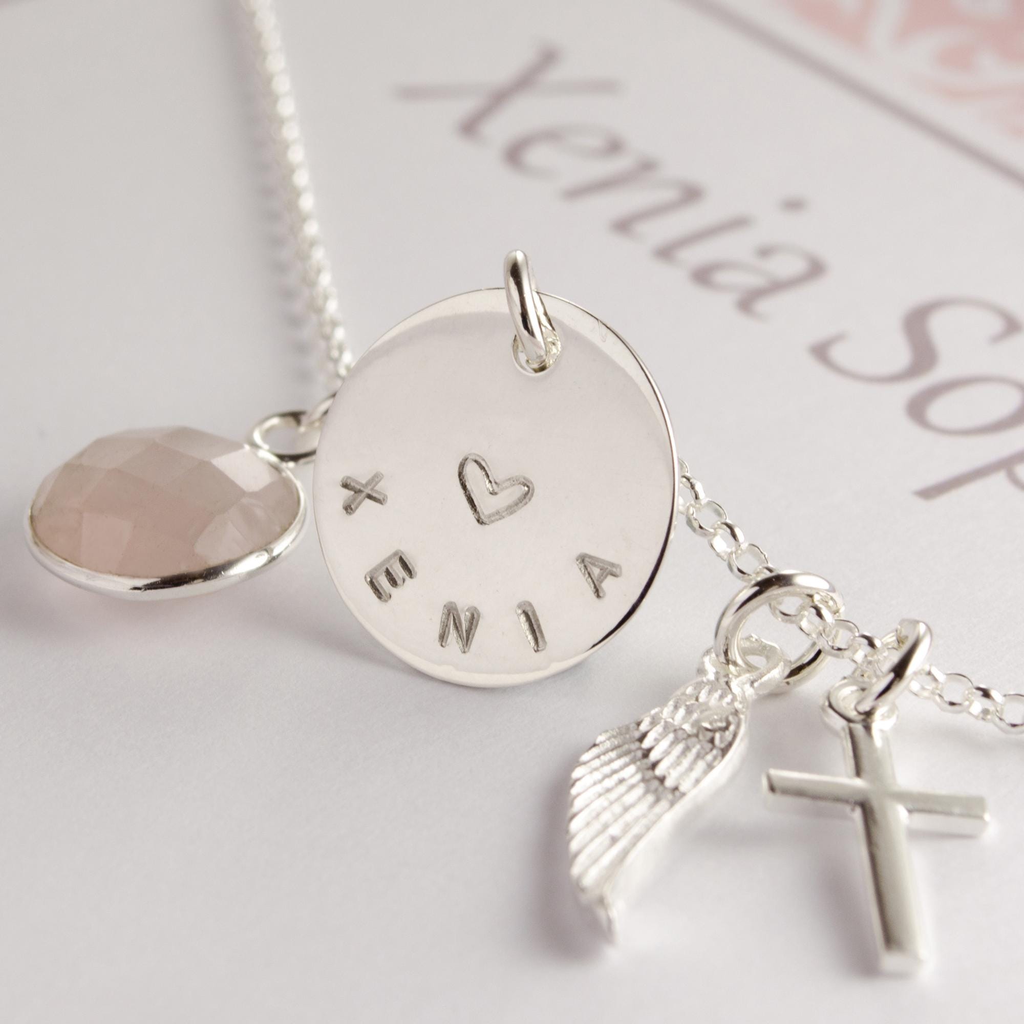 Himmlische Symbole: Detailfoto der Schutzengel-Kette aus 925 Silber, das den Engelsflügel, das Kreuz und den gravierten Namen "Xenia" zeigt.