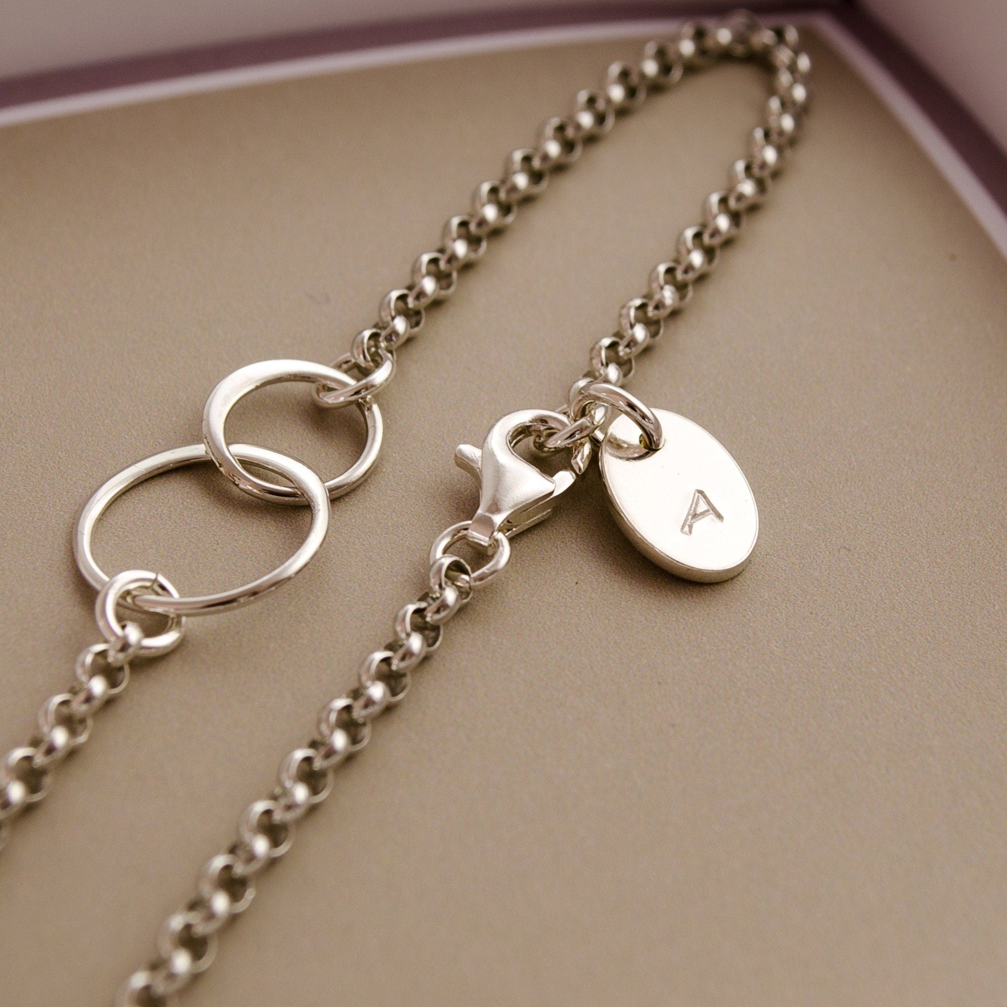 Detailansicht des Initialplättchens am Verschluss und der verschlungenen Ringe als Verbinder am Silberarmband.