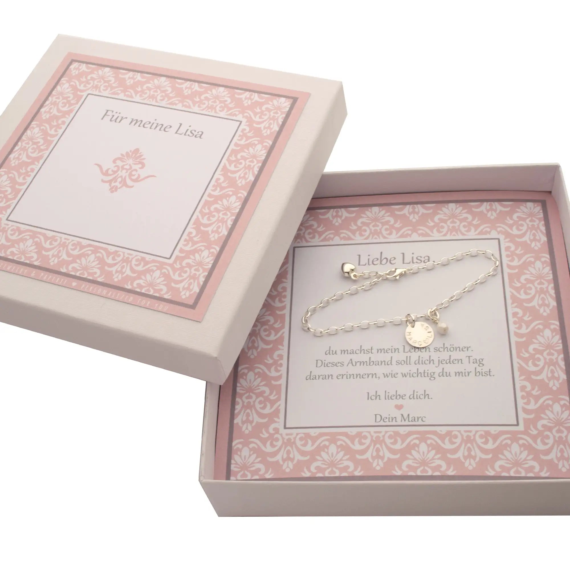 Eine personalisierte Geschenkbox mit weiß-rosa Ornamentmuster zum Hochzeitstag.  Auf einer personalisierten Karte liegt ein 925 Silberarmband mit Namenstaler "Lisa ♡ Marc" und weißer Perle. Das Armband wird zum Hochzeitstag an die Ehefrau verschenkt.