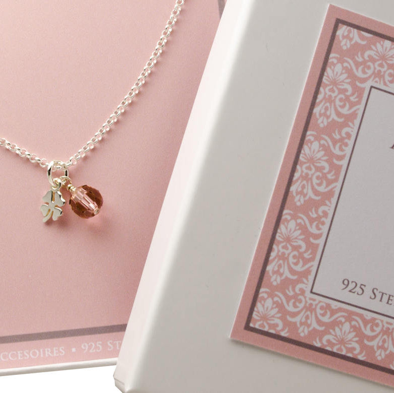 Makroansicht einer zierlichen Gliederkette mit Glücksklee und vintage rose Steinkugel in rosa Geschenkbox.