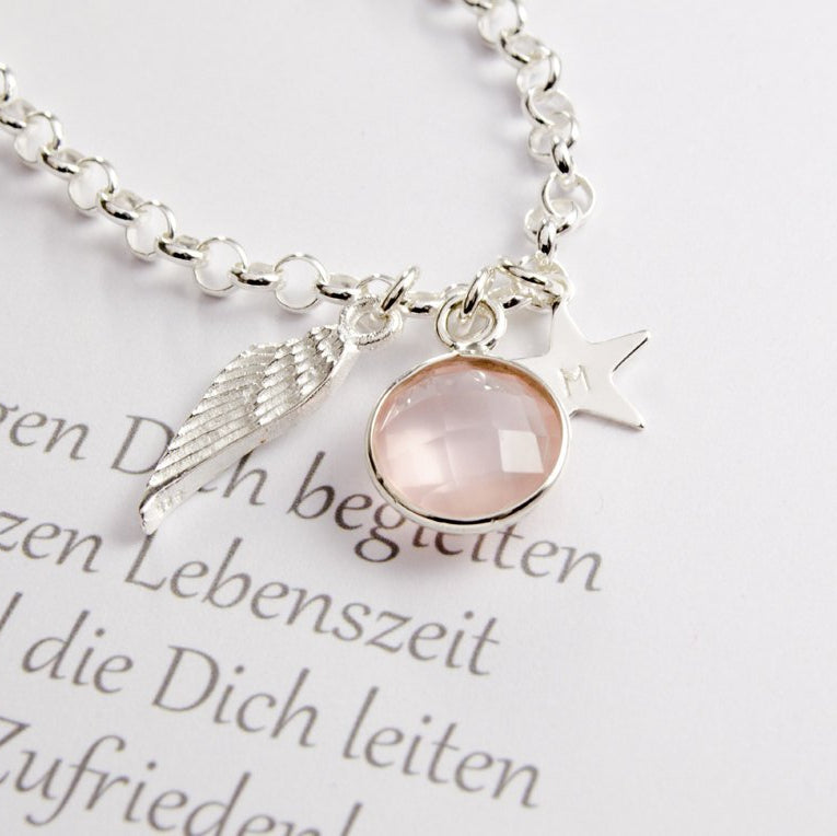 ARMKETTE ZUR TAUFE mit Gravur, Rosenquarz, Flügel, Stern aus 925 Silber. Detailansicht der Anhänger auf Taufspruch liegend.