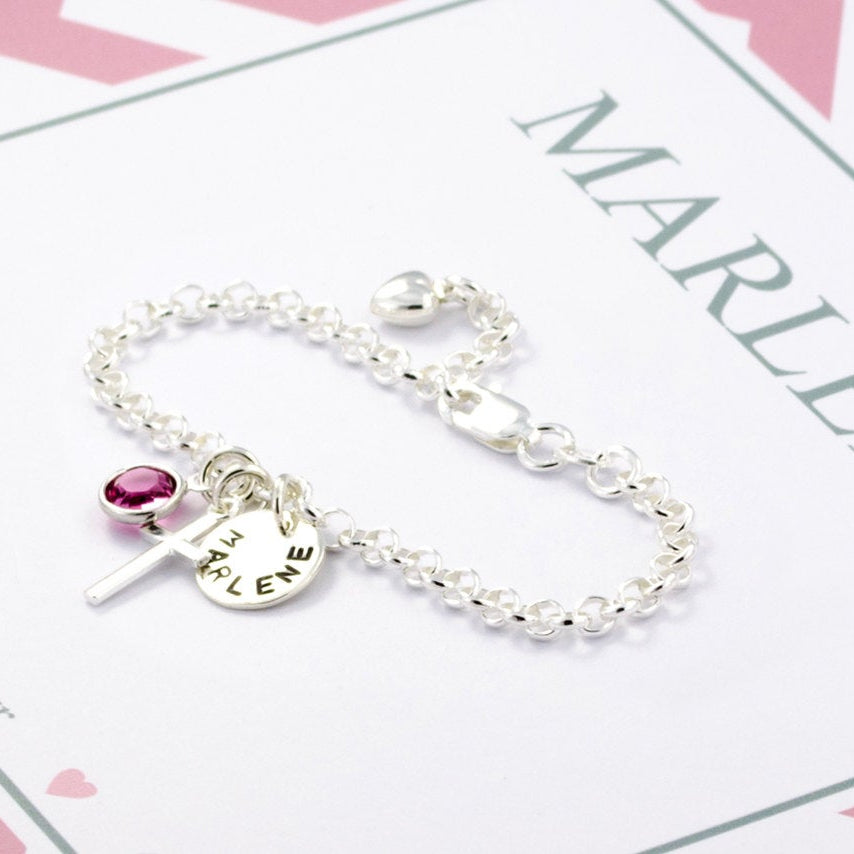Detailansicht eines Silberarmbandes mit rosa Oktober-Stein, Kreuz und Namensplättchen in einer personalisierten Geschenkbox mit rosa Muster.