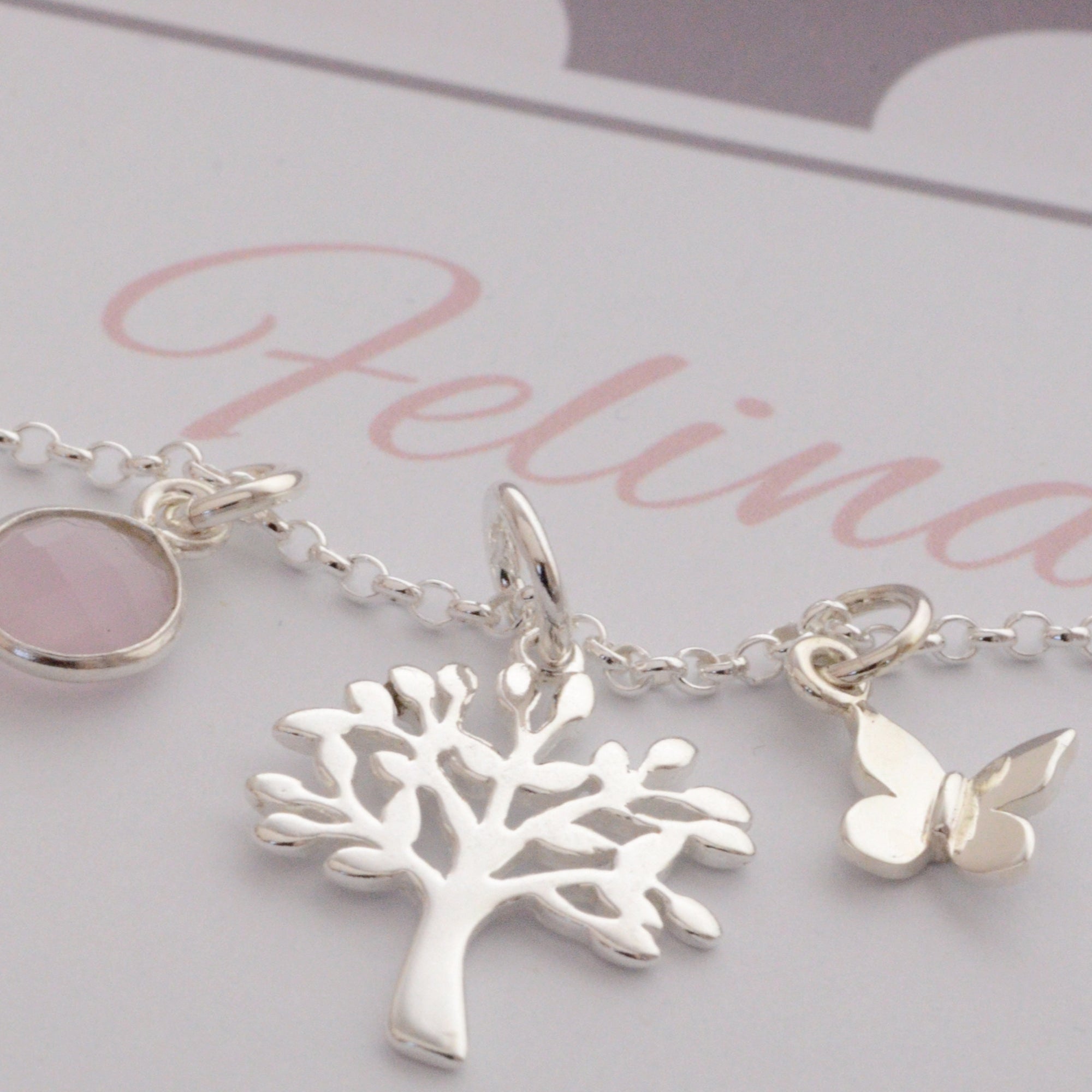 Detailansicht einer filigranen Kette mit drei Anhängern: Rosenquarz in Silber gefasst, Lebensbaum und Schmetterling, aus 925 Sterling Silber. Präsentiert in einer personalisierten Geschenkbox in taupe und rosé.