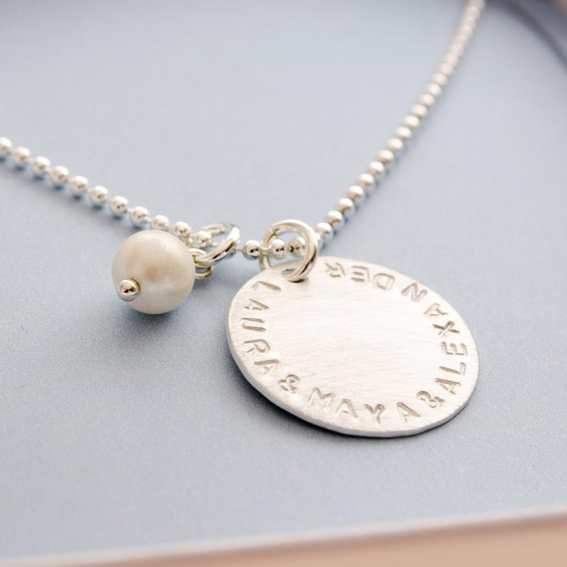 Detailansicht einer Kugelkette mit 18 mm Gravuranhänger mit von Hand gestempelten Namen "LAURA & MAYA & ALEXANDER" in einer kleinen hellblauen Geschenkbox