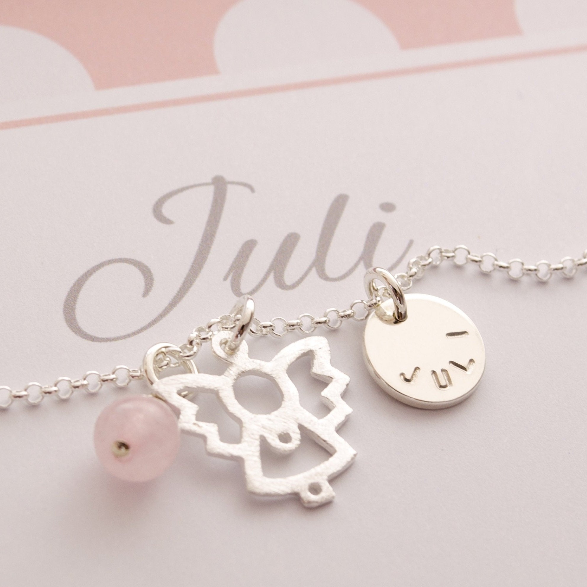 Detailansicht einer Silberkette mit Engel, Rosenquarzkugel und Namensanhänger in einer rosa-weiß gepunkteten, personalisierten Geschenkbox für 'Juli'.