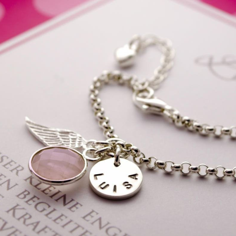 zierliches Gliederamrband mit Verlängerungskettchen und herz. Das Armband hat drei Anhänger: einen runden in Silber gefassten Rosenquarz, einen Engelsflügel und ein rundes Namensplättchen, hier mit den handgestempelten Namen 'LUISA'.
