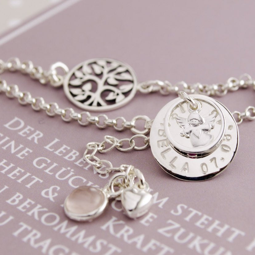 Nahansicht des Silberarmbandes mit Engel im Taufring über dem Namensplättchen, hier für ISABELLA + Datum personalisiert.