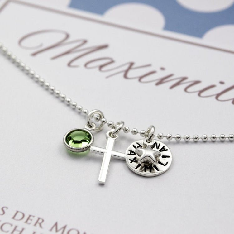 Namenskette 'MEIN GLÜCKSSTERN' mit Wunschgravur, hier MAXIMILIAN, Kreuz, Stern und Monatsstein. Die 925 Sterlingsilber Kette wird in einer blau-grau gepunkteten, personalisierten Geschenkbox von Bloomgart präsentiert.