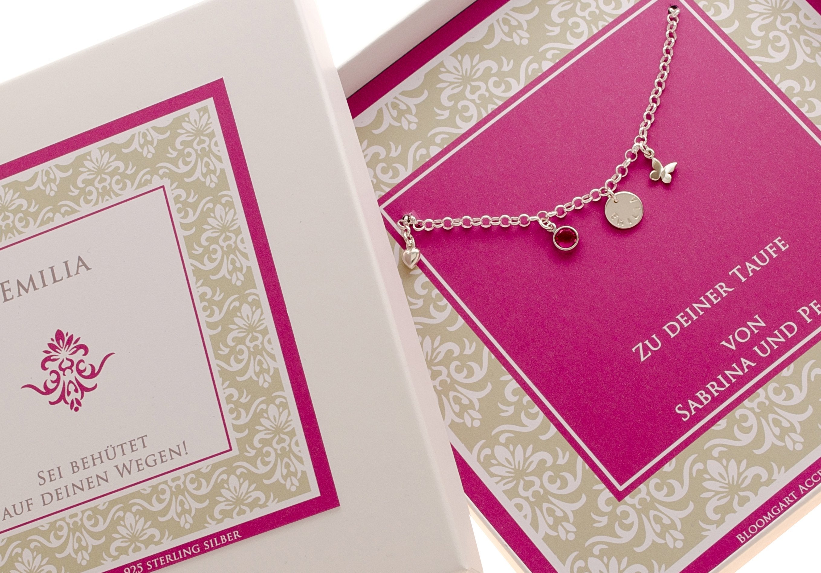 Angeschnittenes Foto einer Geschenkbox mit Ornamentmuster in beige-weiß-pink, personalisiert für den Namen Emilia mit Spruch 'Sei behütet auf deinen Wegen' und Glückwünschen zur Taufe.