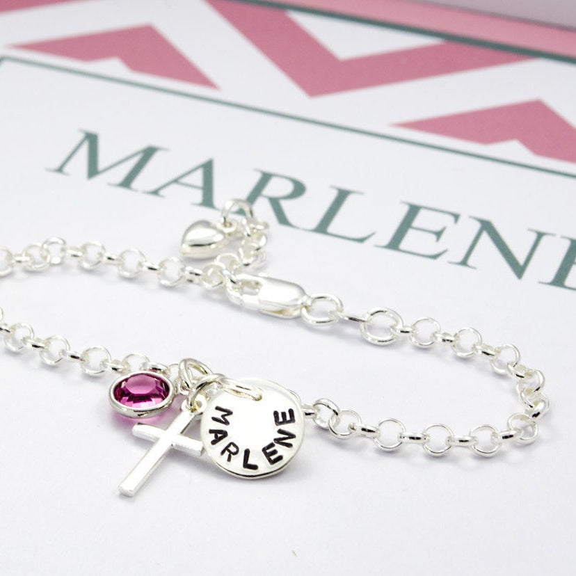 Detailansicht eines Taufarmbandes aus 925 Sterlingsilber mit Namenstaler, Kreuz und Geburtsstein, präsentiert in einer personalisierten rosa-grau-weißen Geschenkbox.