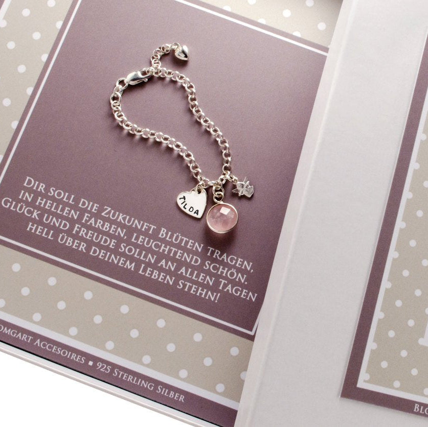 Detailansicht eines sehr süßen Taufarmbandes mit Namensgravur auf einem Herz-Anhänger, Schutzengel und Rosenquarz. Das Armband ist in der Länge verstellbar und liegt in einer personalisierten Geschenkbox in weiß-beige-braun Tönen im Pünktchen Design.