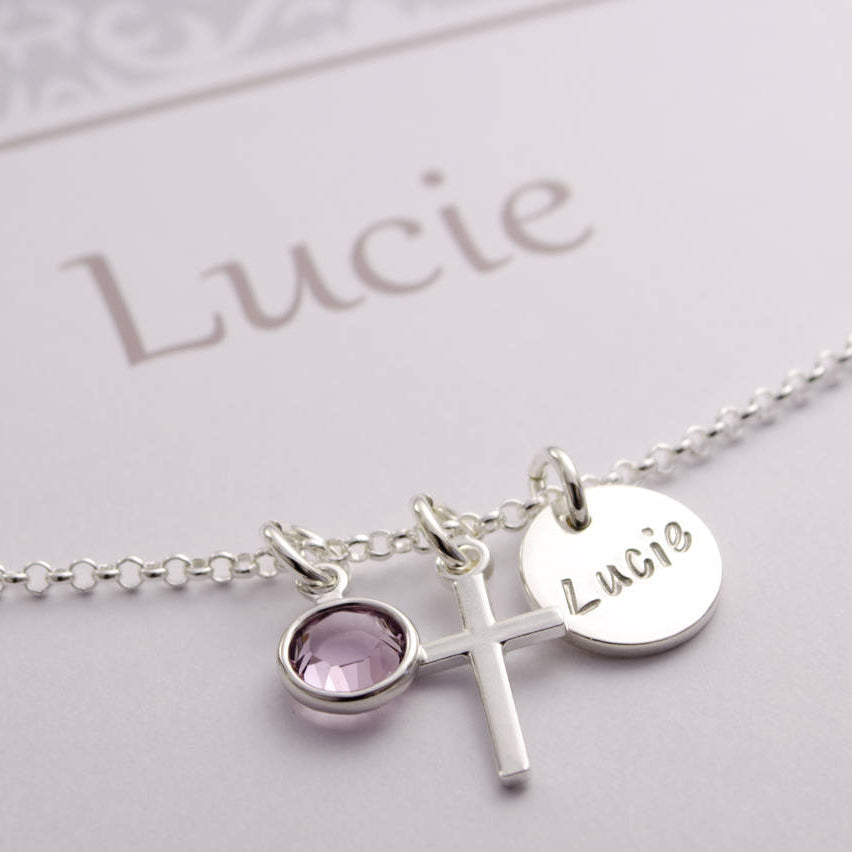 Detailansicht der filigranen kreuzkette aus 925 Silber mit Namenstaler, hier 'Lucie', Kreuz und Monatsstein,  in einer eleganten grau-weißen Geschenkbox mit Ornamentmuster, personalisiert von Bloomgart.