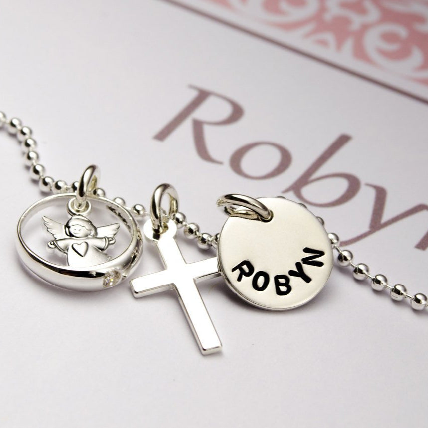 Makroaufnahme einer 925 Sterlingsilber Kugelkette mit handgestempeltem Namenstaler, Kreuz und Schutzengel im Taufring.